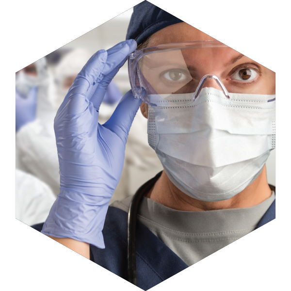 A person looking at the viewer. They are wearing PPE in the form of protective glasses, surgical mask, and gloves.